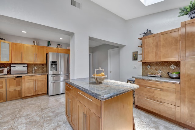 kitchen with light stone countertops, stainless steel refrigerator with ice dispenser, tasteful backsplash, and a kitchen island