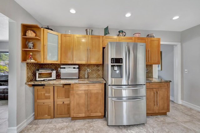 kitchen with stainless steel fridge, backsplash, light stone counters, and light tile patterned floors