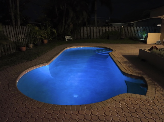 pool at night featuring a patio