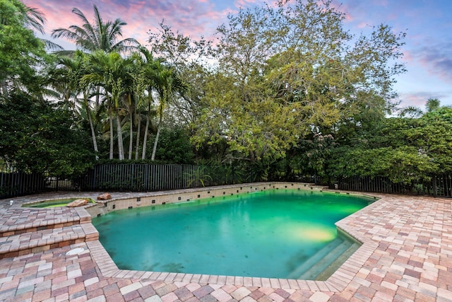 pool at dusk featuring a patio and a hot tub