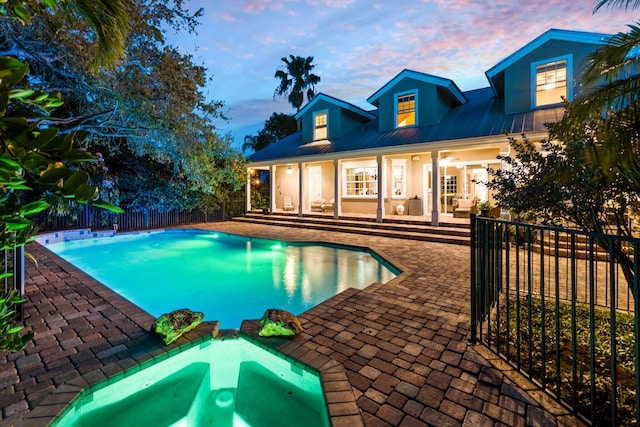 pool at dusk with an in ground hot tub and a patio area