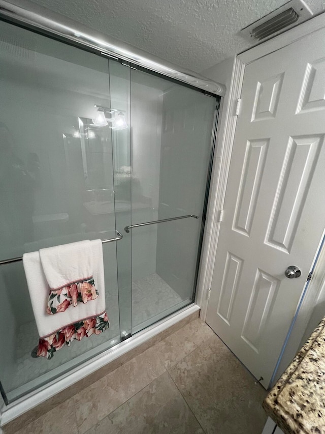 bathroom with an enclosed shower, a textured ceiling, and tile floors