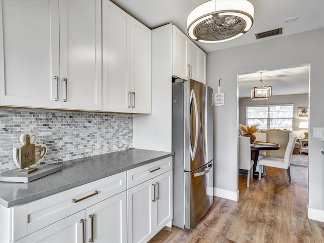 kitchen with backsplash, stainless steel refrigerator, white cabinets, and light wood-type flooring