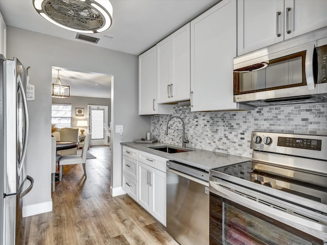 kitchen with white cabinetry, sink, light hardwood / wood-style flooring, stainless steel appliances, and tasteful backsplash