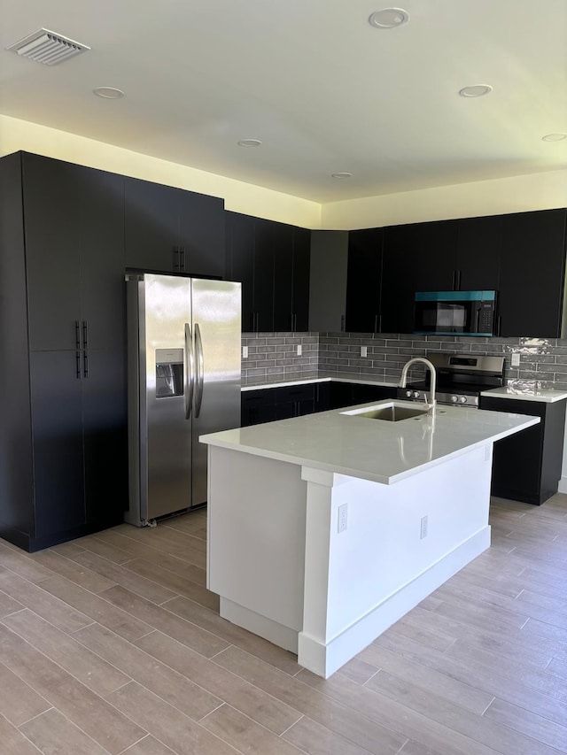 kitchen with appliances with stainless steel finishes, a center island with sink, light hardwood / wood-style floors, and sink