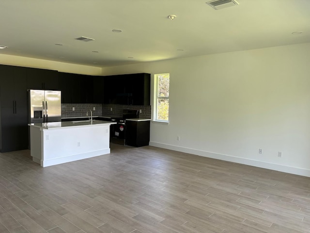 kitchen featuring tasteful backsplash, black electric range oven, stainless steel fridge, a kitchen island with sink, and light wood-type flooring