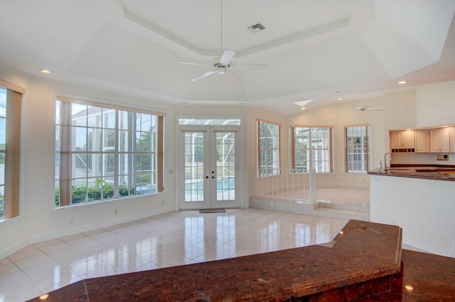 interior space with a raised ceiling, french doors, ceiling fan, and light tile floors