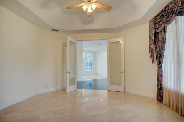 tiled empty room with ceiling fan, a tray ceiling, and french doors