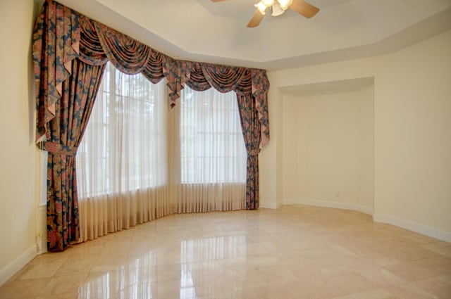 spare room with a tray ceiling, ceiling fan, light tile floors, and a wealth of natural light