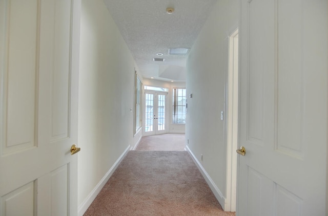 hallway with french doors, a textured ceiling, and light colored carpet