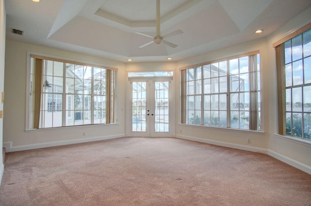 unfurnished sunroom with a healthy amount of sunlight, a raised ceiling, ceiling fan, and french doors