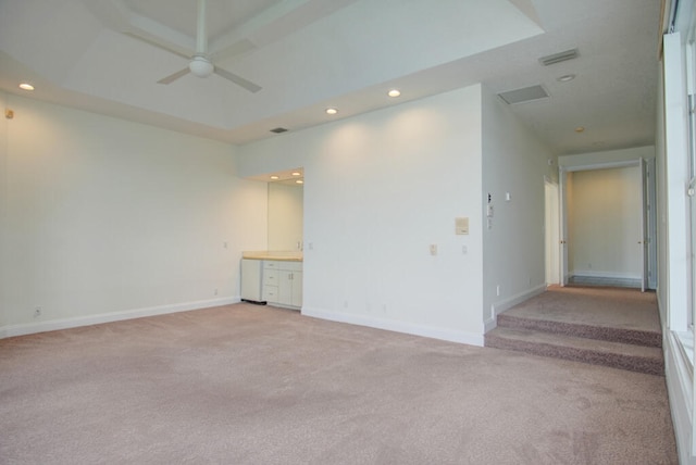 spare room with a raised ceiling, light carpet, and ceiling fan