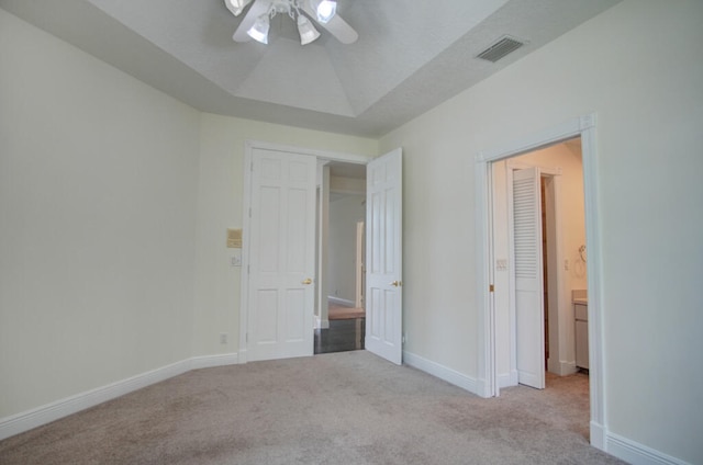 unfurnished bedroom featuring a raised ceiling, light colored carpet, and ceiling fan