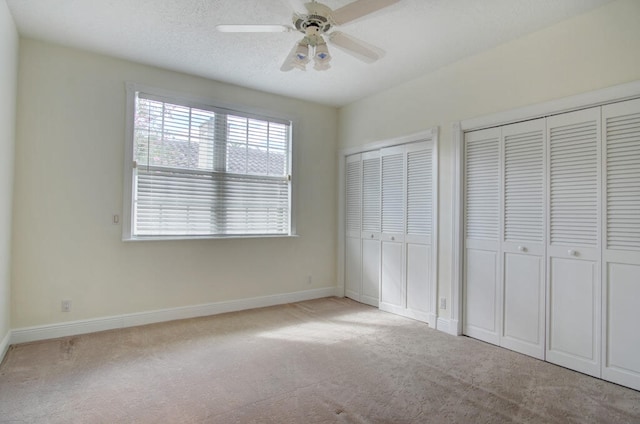 unfurnished bedroom featuring light colored carpet, ceiling fan, and multiple closets