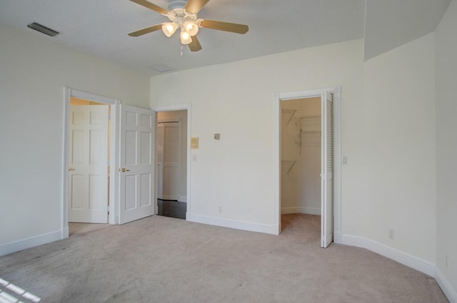 unfurnished bedroom with light carpet, a closet, a walk in closet, and ceiling fan