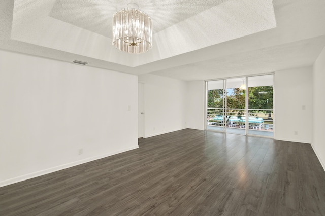 spare room featuring a raised ceiling, an inviting chandelier, expansive windows, and dark wood-type flooring