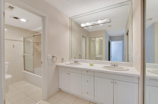 full bathroom featuring tile patterned flooring, double sink vanity, shower / bath combination with glass door, a textured ceiling, and toilet