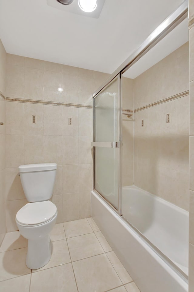 bathroom with shower / bath combination with glass door, toilet, tile patterned floors, and tile walls