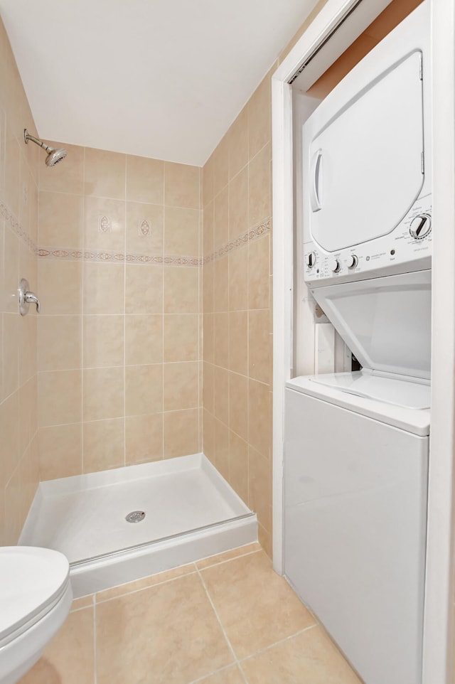 bathroom with stacked washer and dryer, toilet, a tile shower, and tile patterned flooring