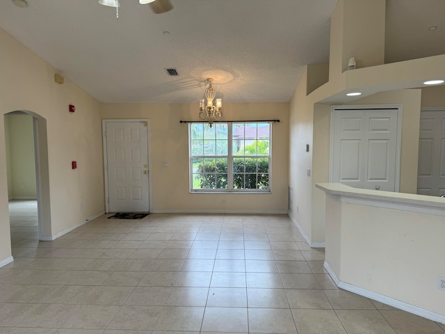 empty room featuring light tile floors, a textured ceiling, ceiling fan with notable chandelier, and vaulted ceiling