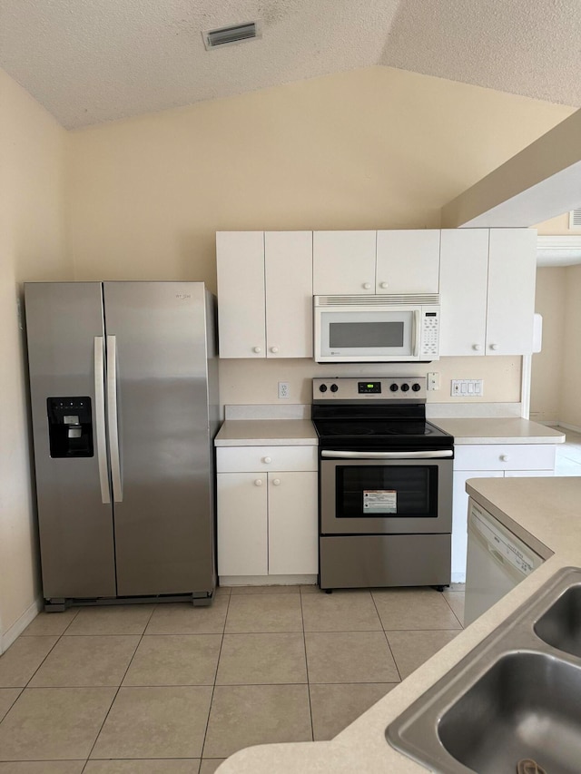 kitchen with light tile floors, appliances with stainless steel finishes, white cabinetry, and vaulted ceiling