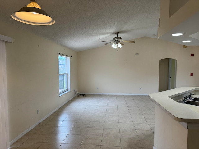 unfurnished room with light tile flooring, vaulted ceiling, ceiling fan, and a textured ceiling