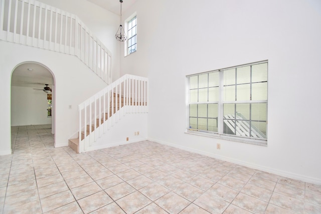 tiled spare room with a towering ceiling, ceiling fan with notable chandelier, and a healthy amount of sunlight