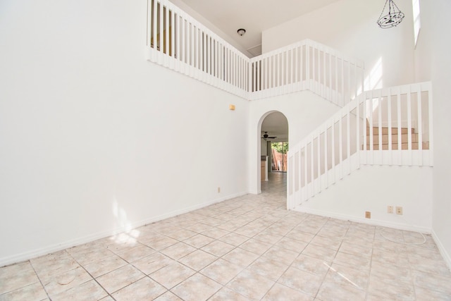 tiled empty room featuring ceiling fan and a high ceiling