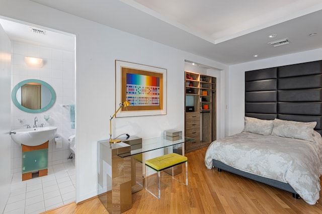 bedroom featuring a spacious closet, connected bathroom, hardwood / wood-style flooring, and tile walls