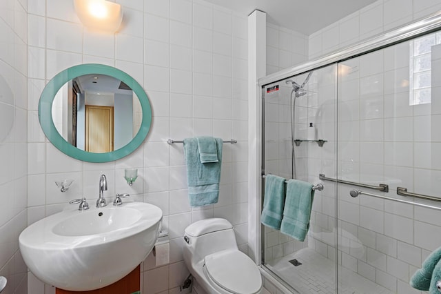 bathroom featuring toilet, tasteful backsplash, a shower with shower door, and tile walls