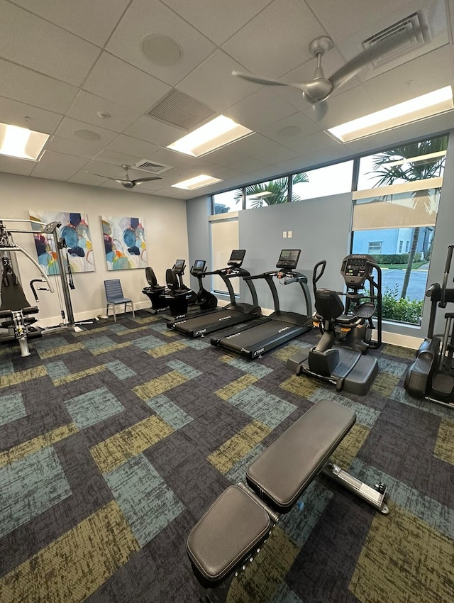 workout area featuring ceiling fan, a drop ceiling, and dark carpet