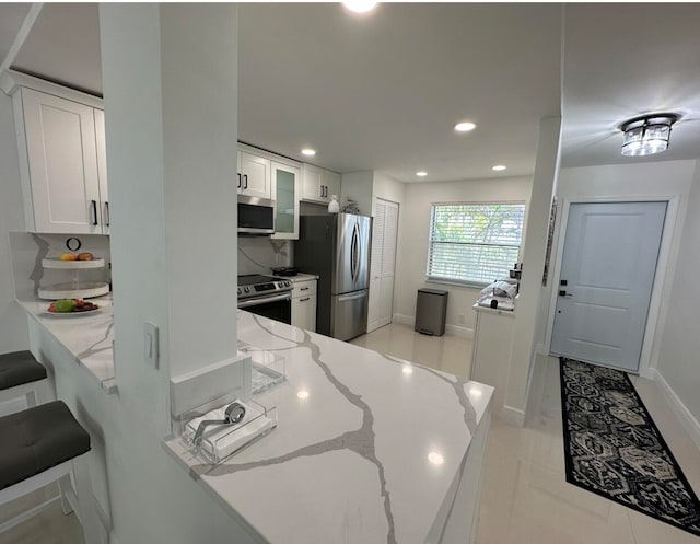 kitchen with light stone countertops, stainless steel appliances, light tile floors, white cabinets, and a breakfast bar area