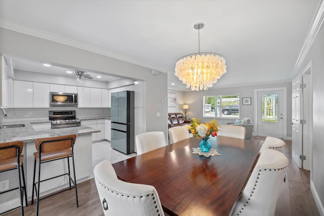 dining room featuring ceiling fan with notable chandelier, light hardwood / wood-style flooring, ornamental molding, and sink