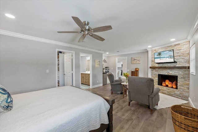 bedroom featuring ensuite bath, ornamental molding, ceiling fan, wood-type flooring, and a stone fireplace