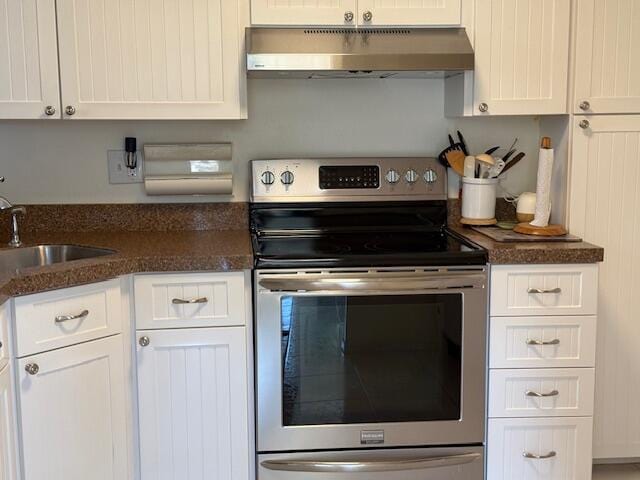 kitchen with dark stone countertops, stainless steel electric stove, a sink, under cabinet range hood, and white cabinetry