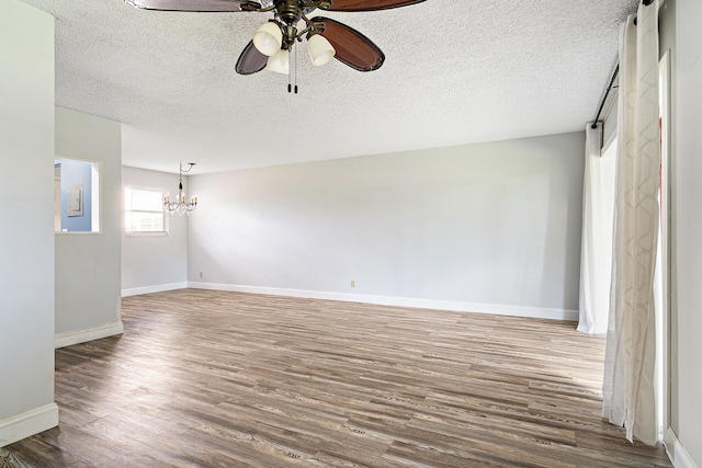 empty room with hardwood / wood-style floors, ceiling fan with notable chandelier, and a textured ceiling