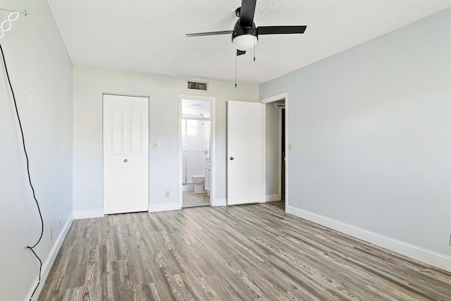 unfurnished bedroom with ensuite bath, ceiling fan, light hardwood / wood-style floors, a textured ceiling, and a closet