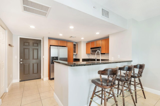 kitchen with light tile flooring, a breakfast bar area, stainless steel appliances, and kitchen peninsula