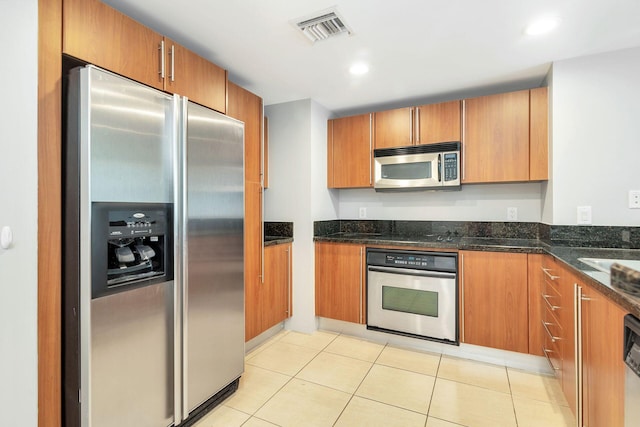 kitchen with dark stone counters, stainless steel appliances, and light tile floors