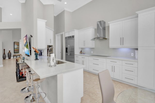 kitchen featuring wall chimney exhaust hood, white cabinetry, light tile patterned floors, appliances with stainless steel finishes, and a towering ceiling