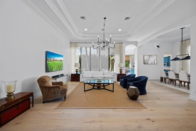 living room featuring an inviting chandelier, light wood-type flooring, crown molding, and a tray ceiling