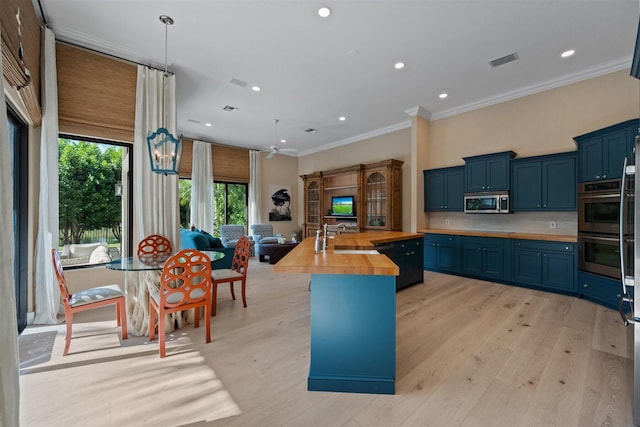 kitchen featuring tasteful backsplash, hanging light fixtures, wood counters, stainless steel appliances, and an island with sink