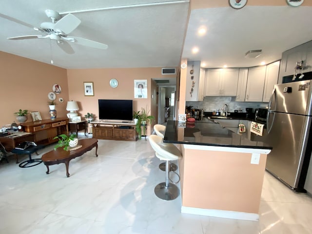 kitchen with kitchen peninsula, ceiling fan, light tile floors, stainless steel refrigerator, and tasteful backsplash