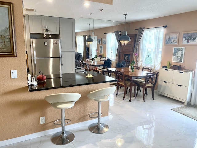 kitchen with stainless steel fridge, gray cabinetry, hanging light fixtures, a breakfast bar area, and light tile flooring