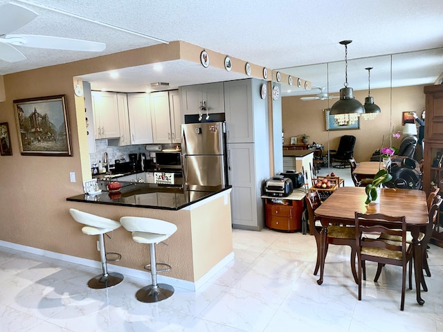 kitchen with stainless steel appliances, light tile floors, ceiling fan, kitchen peninsula, and hanging light fixtures