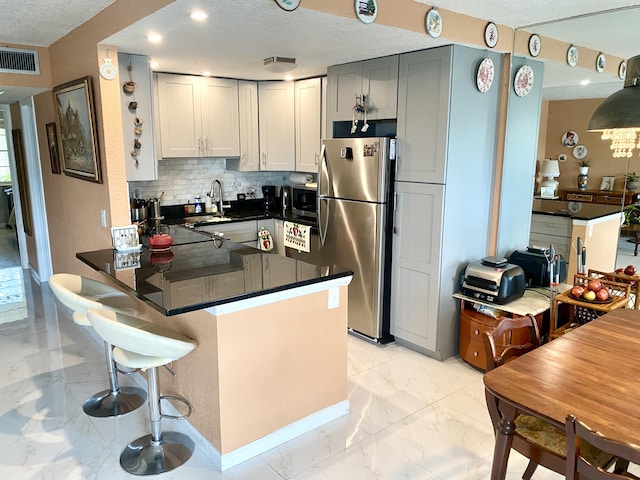 kitchen with kitchen peninsula, stainless steel fridge, light tile floors, gray cabinetry, and backsplash