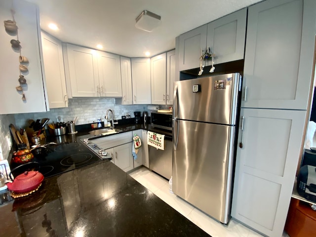 kitchen with light tile floors, dark stone counters, tasteful backsplash, stainless steel fridge, and sink