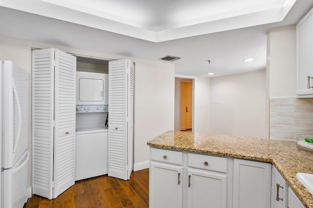 kitchen with white fridge, light stone countertops, stacked washer / dryer, white cabinetry, and dark wood-type flooring