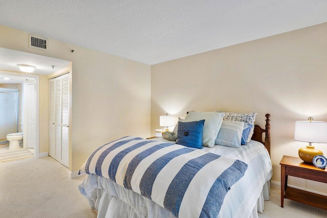 carpeted bedroom featuring a closet, ensuite bath, and a textured ceiling