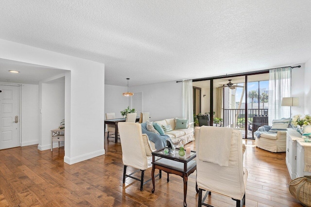 living room featuring ceiling fan, wood-type flooring, a textured ceiling, and a wall of windows